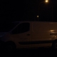 Tradesperson's van in dark, shadowy street at dusk.